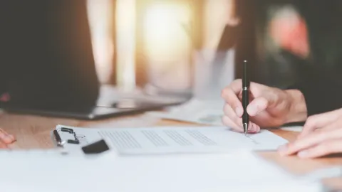 Deux personnes signant un document sur une table, devant un ordinateur portable